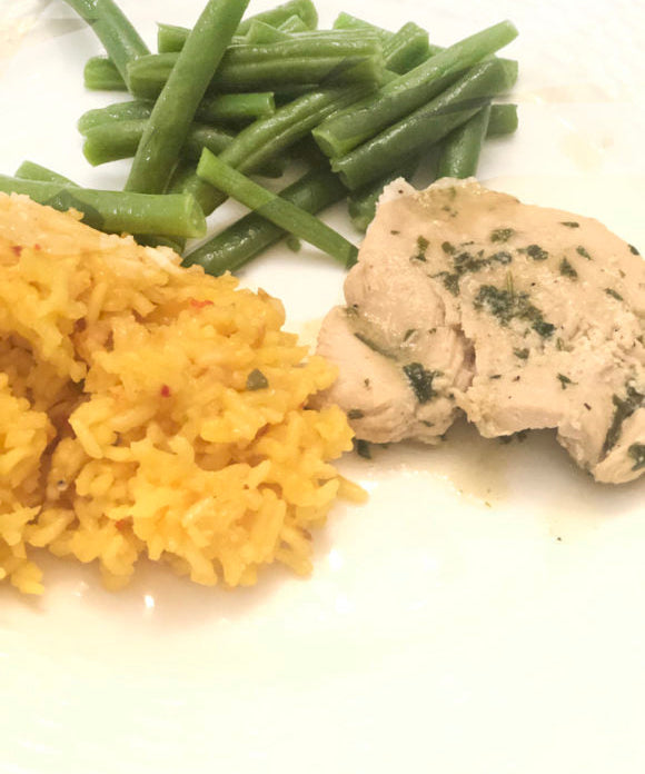 chicken thighs topped marinated in lime and cilantro with green beans and rice on a white plate