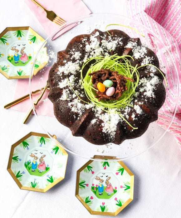 chocolate easter cake with edible green grass and chocolate bird nest on top with easter plates gold forks pink napkins