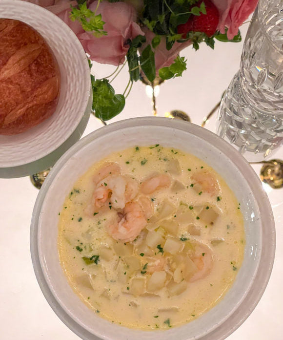 shrimp chowder on table in white bowl with bread on plate beside bowl