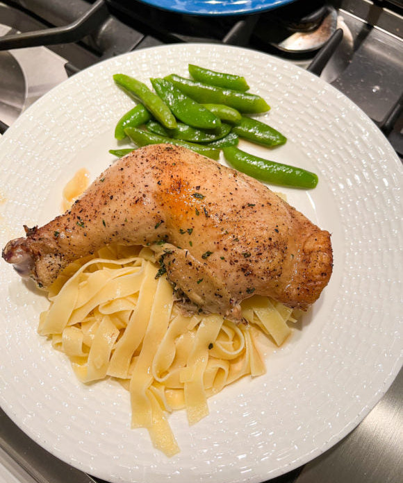 whole baked chicken leg with egg noodles and sugar snap peas on a white plate
