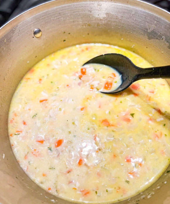 creamy chicken soup in a pot being stirred with large black spoon