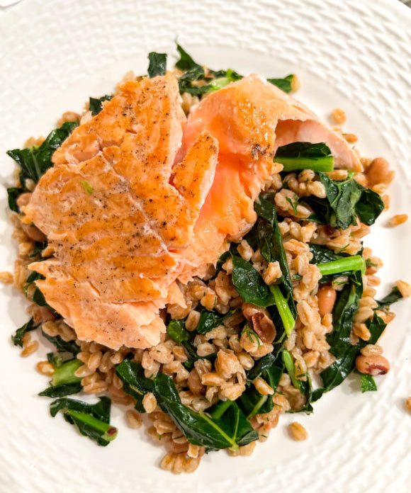 salmon served over a bed of farro with kale and black eyed peas