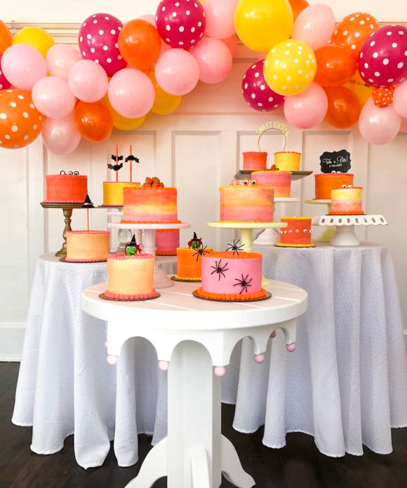 halloween cakes on 3 round tables with balloon garland in the background
