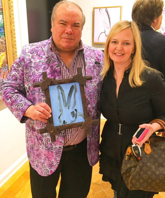 hunt slonem holding blue bunny painting with blonde lady beside him