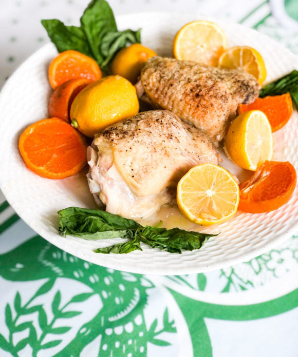 baked chicken on white plate with orange and lemon slices and basil