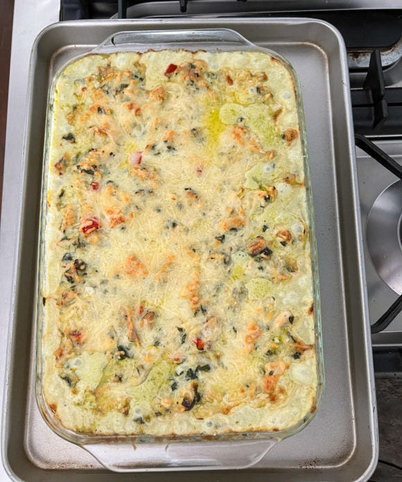 chicken casserole with spinach and artichokes in a 9x13 glass casserole dish on top of a cookie tray on a stove