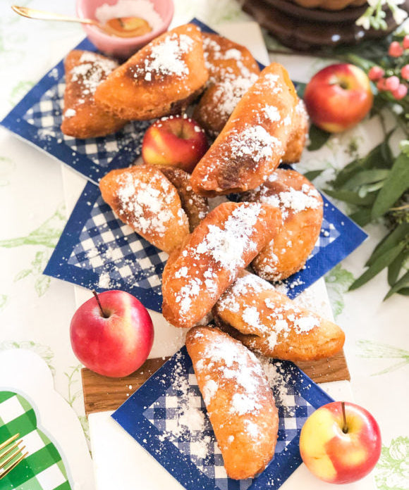 fried apple pies with powdered sugar placed on blue and white gingham napkins with whole apples