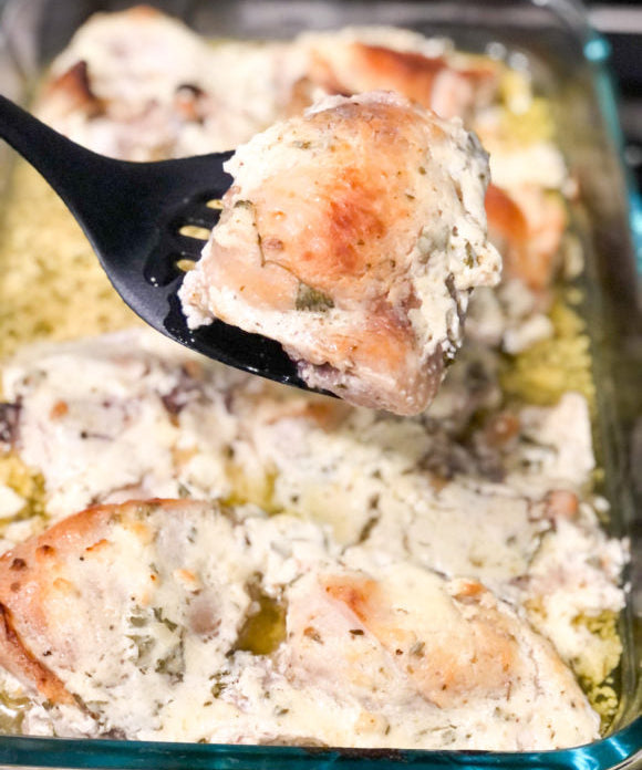 baked chicken thighs marinated with plain yogurt in casserole dish with one piece being held on a black spatula