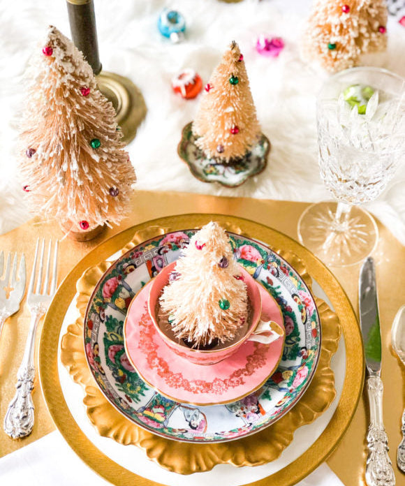 pink and gold christmas table setting with bottle brush trees and colorful ornaments