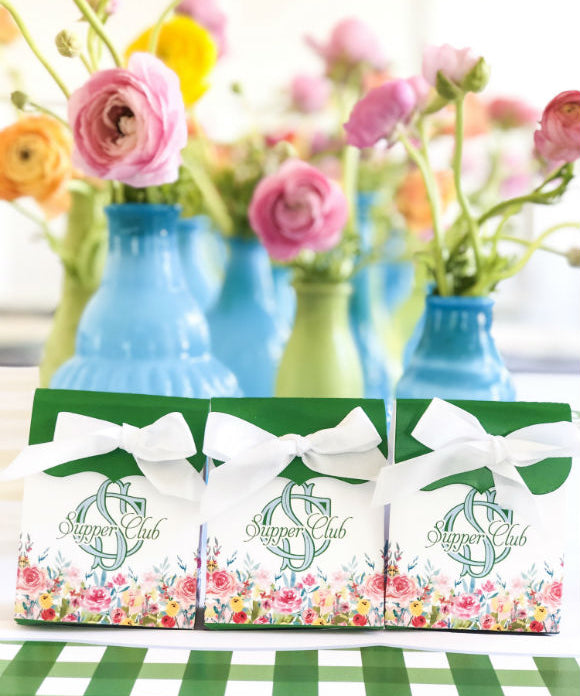 table set with green and white gingham placemats flowers in blue vases and favor boxes