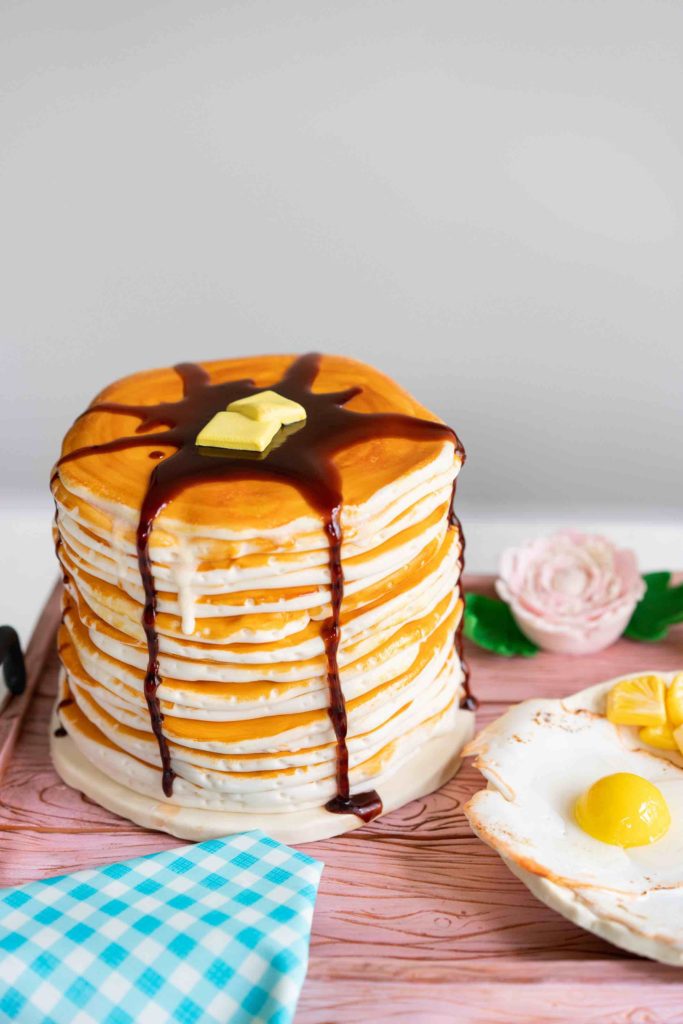 a cake that looks like breakfast in bed with a stack of pancakes eggs and toast