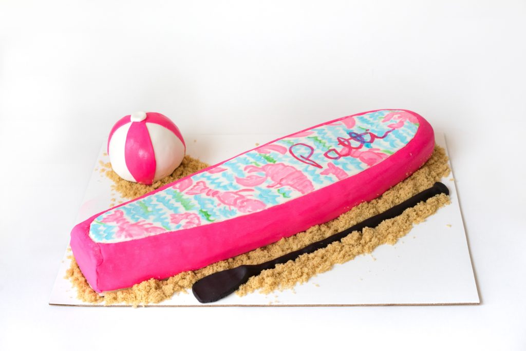 Lilly Pulitzer paddle board cake with the Lilly Lobster Print pattern and a beach ball and paddle made of fondant