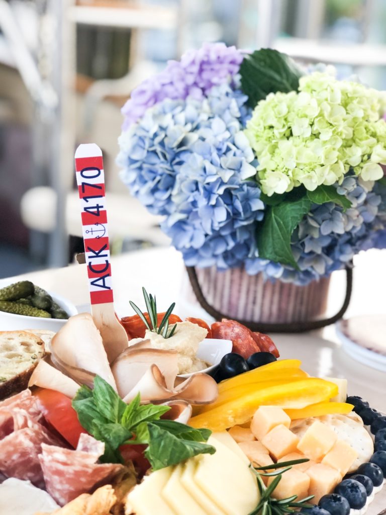 Cheese board charcuterie with nantucket basket full of pink blue green and purple hydrangeas with red and white striped fork