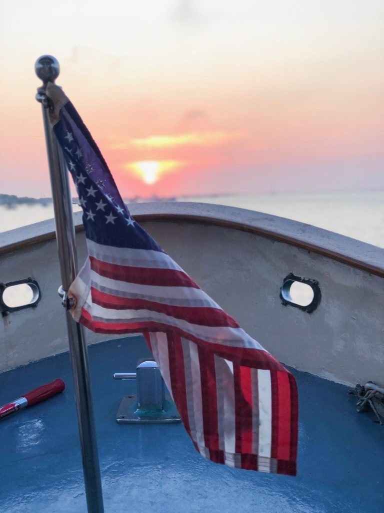 American flag on front of boat with sunset behind it