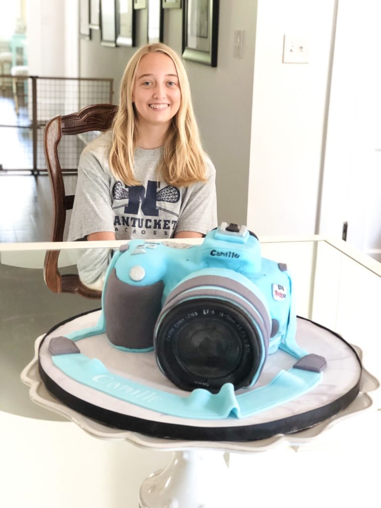 blue sculpted camera cake with custom name on camera strap with birthday girl in photo
