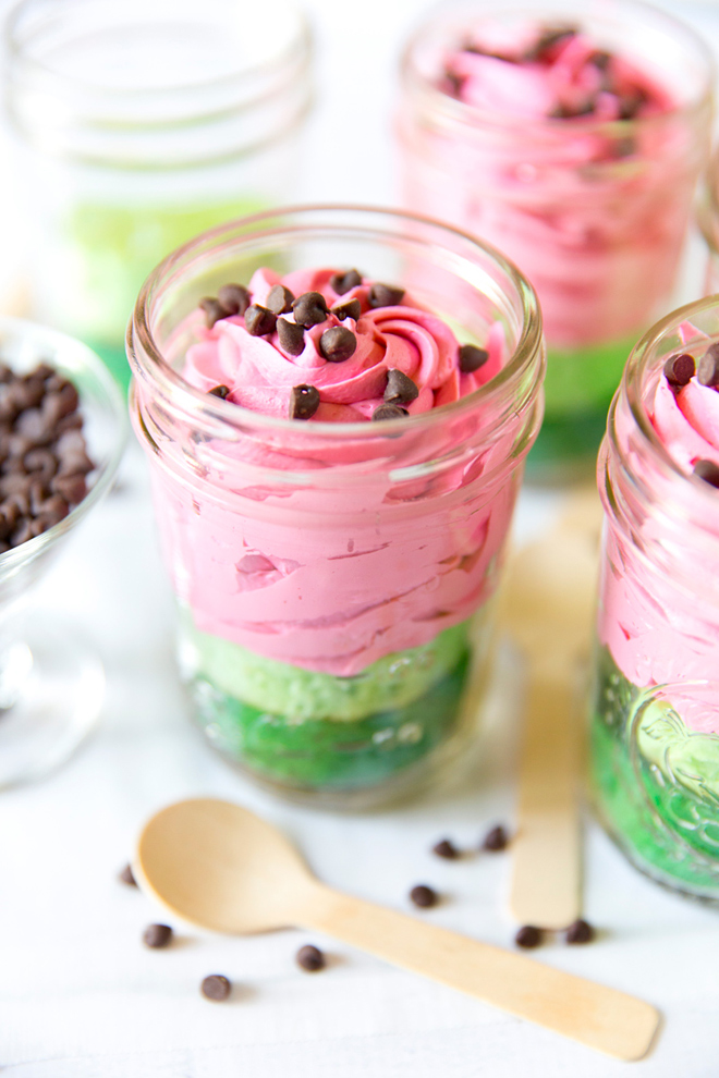 mini watermelon cake in mason jar with layers of green cake and pink frosting with chocolate chips for seeds