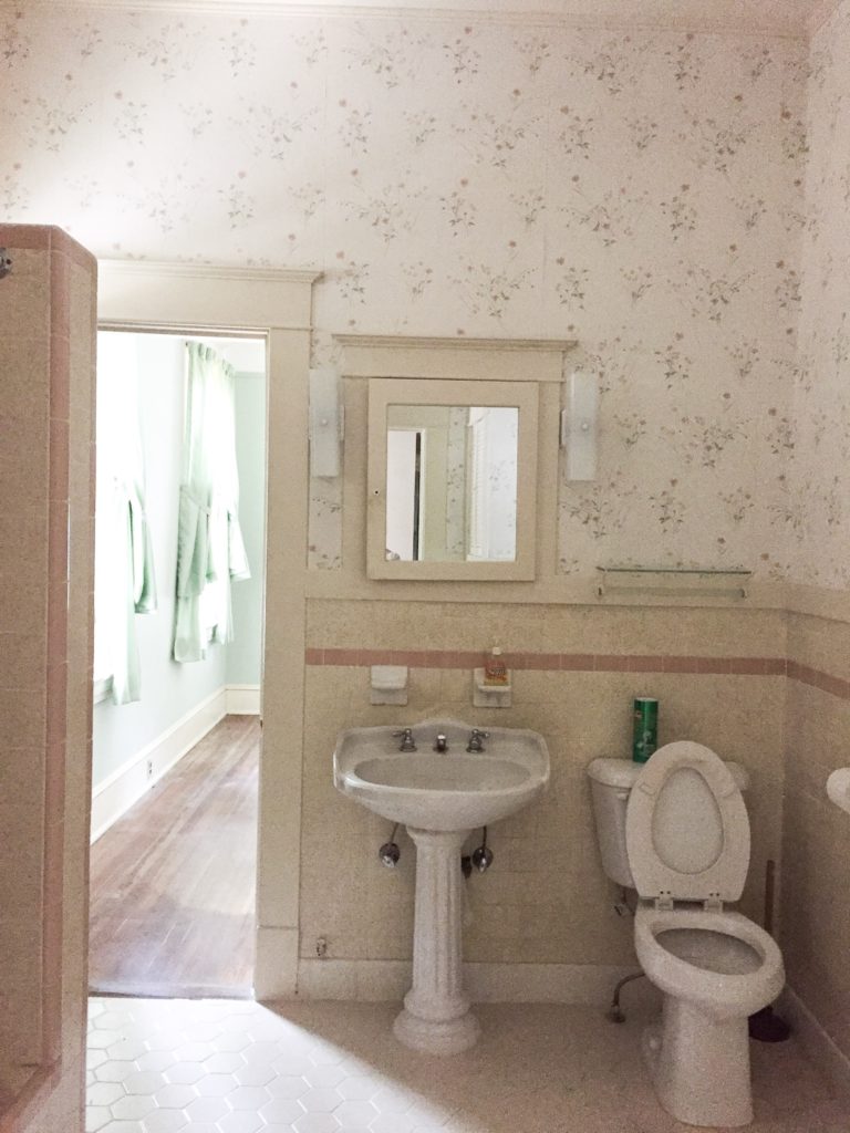 vintage bathroom with wallpaper on half wall and wood trim on bottom half of wall