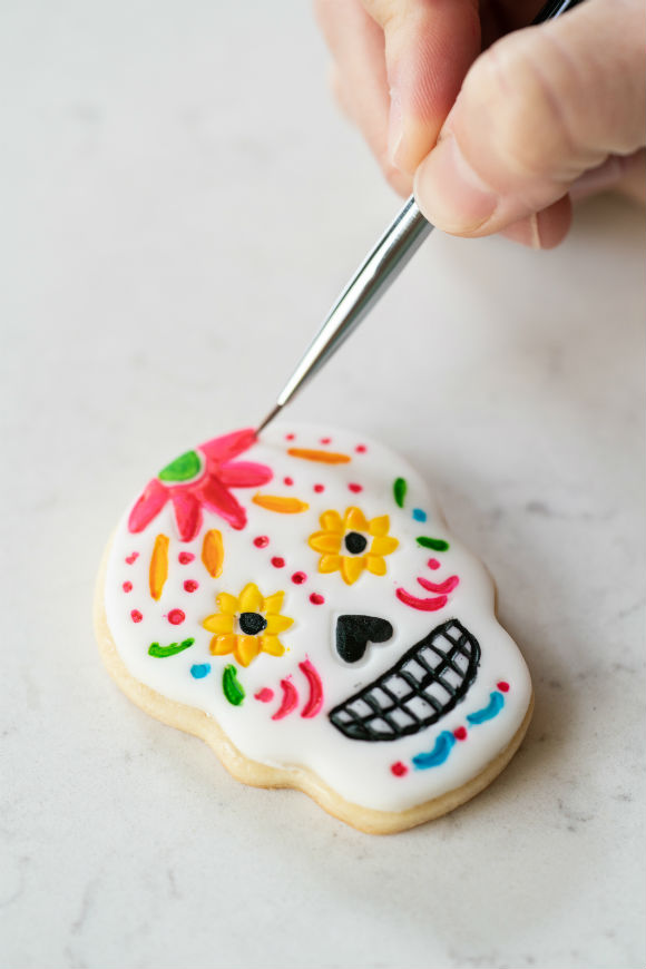 Skull cookie being painted with paint brush with bright colors and flowers