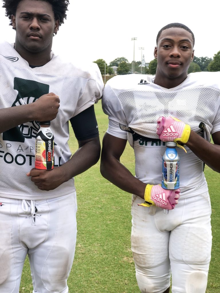 2 football players holding body armor sports drink vertically between their fists