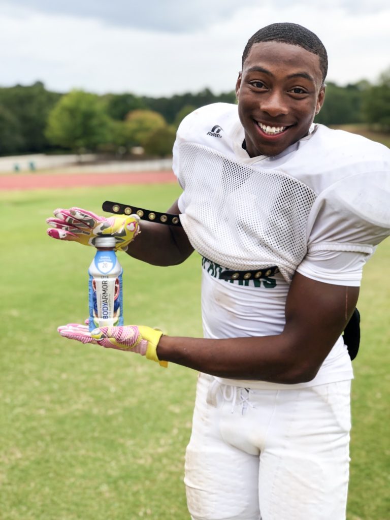 football player holding a BODYARMOR sports drink in his open palms and smiling