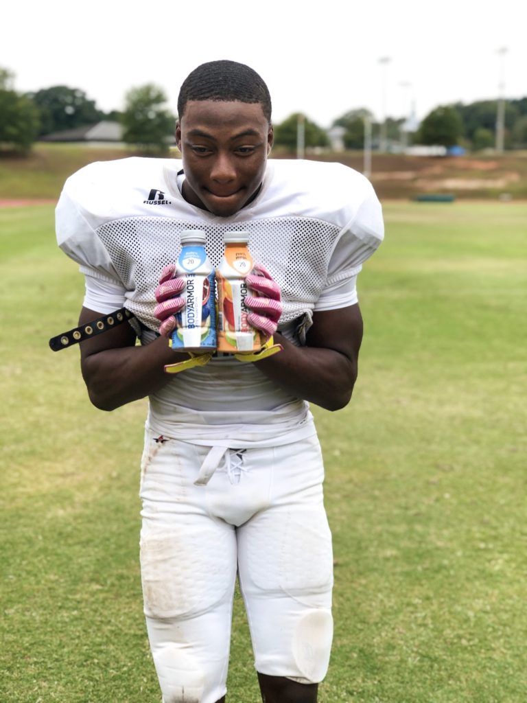 football player holding 2 bottles of bodyarmor sports drink close to his chest