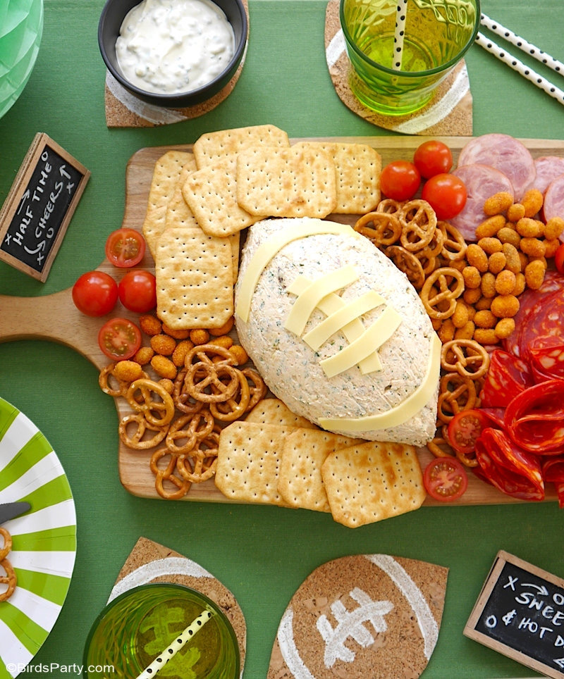 football shaped cheese dip on wooden board with crackers pretzels and vegetables