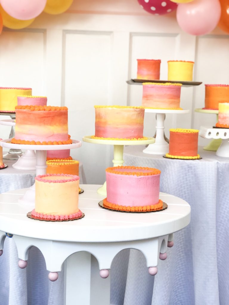 pink yellow orange peach colored cakes in a group on round tables