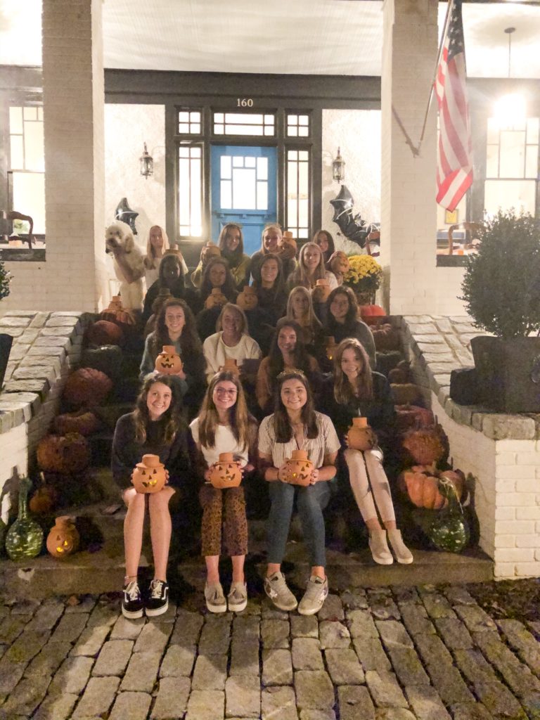 group of teen girls sitting on front porch steps holdling jack o lanterns