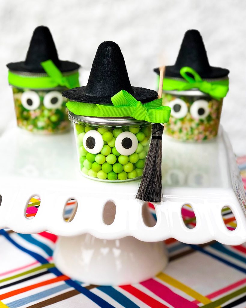 small glass jars filled with green candies and candy eyes topped with a witch hat and mini broom