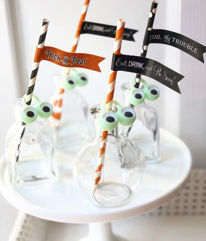 glass bottles with Halloween straws and straw flags and monster eye rings on the rim 