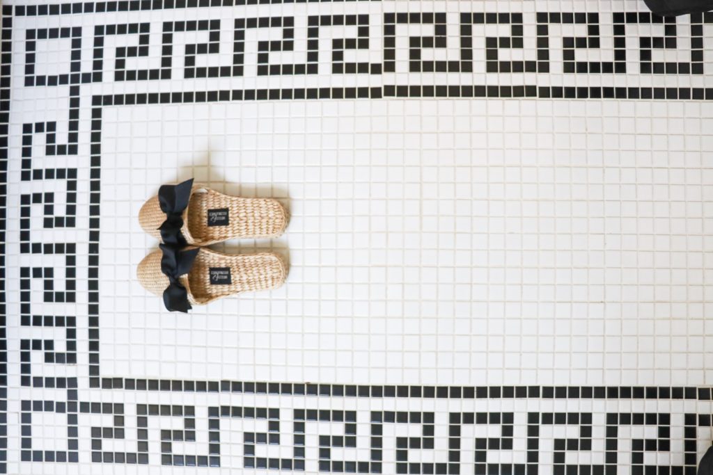 white tile bathroom floor with black greek key pattern and wicker slippers with bows