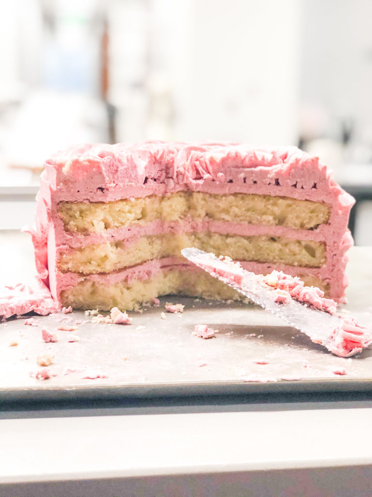 vanilla cake with pink frosting partially sliced with cake knife on counter