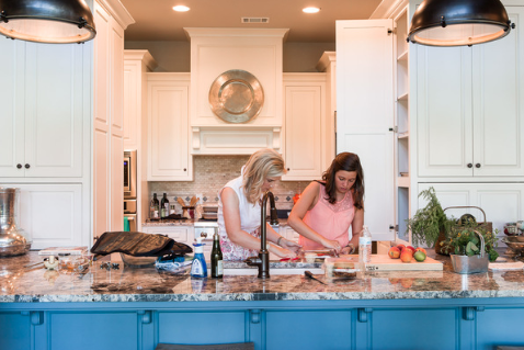 ivy odom and rebecca lang cooking in a white kitchen with blue island