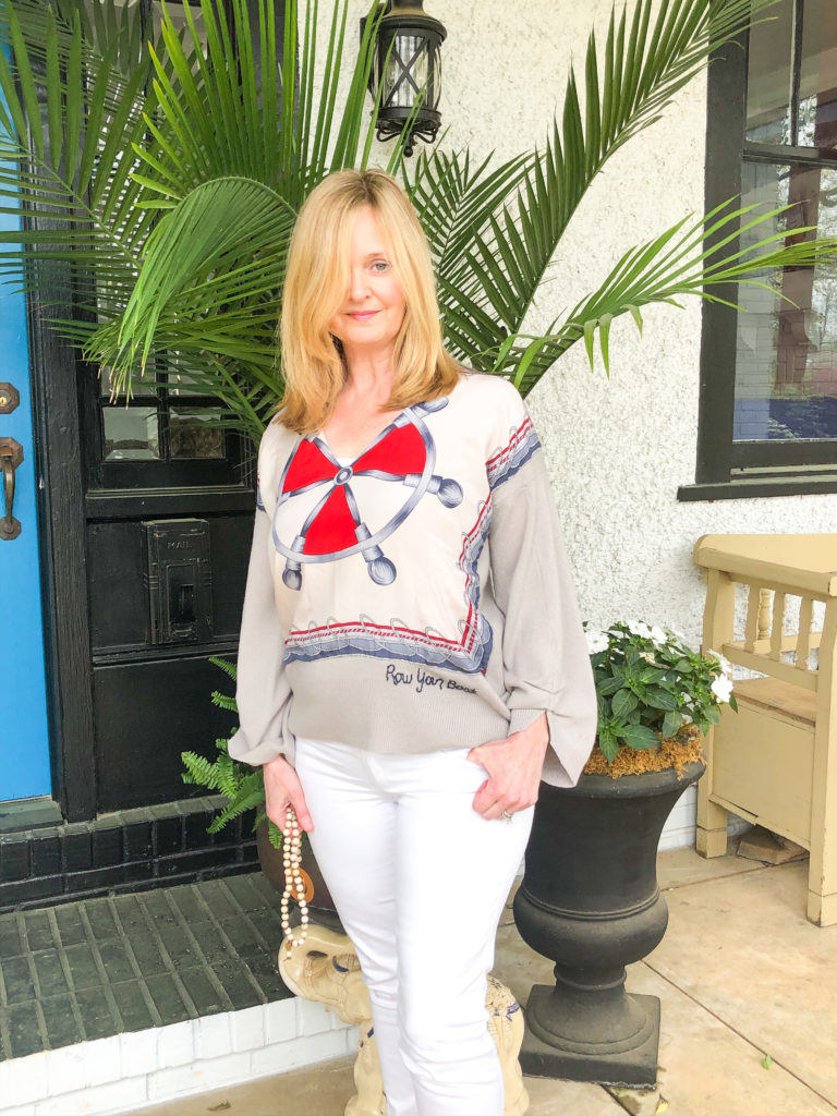 blonde lady with white jeans and sweater standing in front of palm tree on front porch