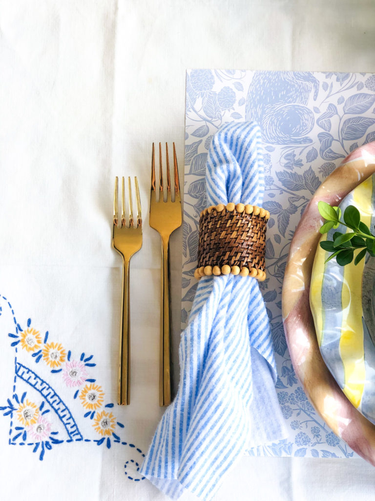 table setting with napkin in brown napkin ring gold flatware ruffled plte edges blue floral placemats