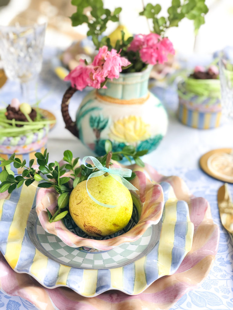table set with pastel pottery dishes with ruffled edges and a pear and azaleas
