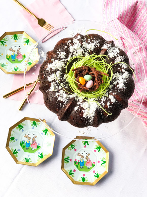 chocolate easter cake with edible green grass and chocolate bird nest on top with easter plates gold forks pink napkins