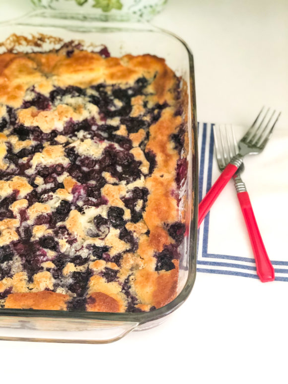 blueberry cobbler with two red forks beside glass pan on shite napkin with blue stripes