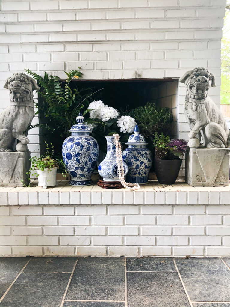 white outdoor fireplace with blue and white vases and concrete foo dogs
