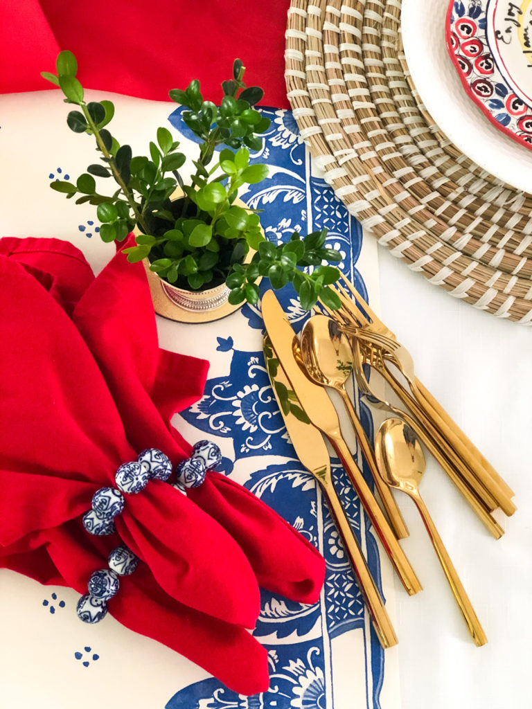 red napkins with blue and white bead napkin rings and gold forks with boxwood leaves in silver cup