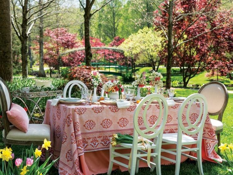 table set in flowering garden white chairs coral colored tablecloth
