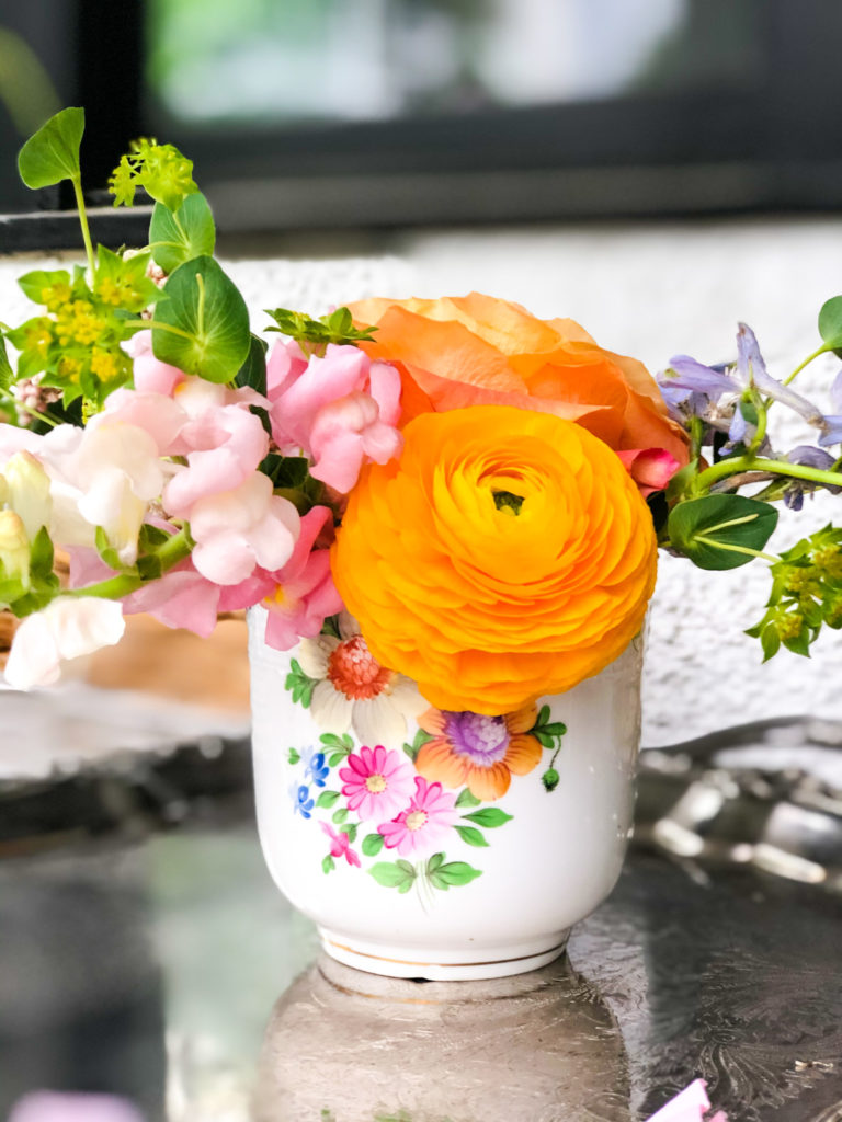 orange ranunculus blooms and snapdragons in white vase with floral design