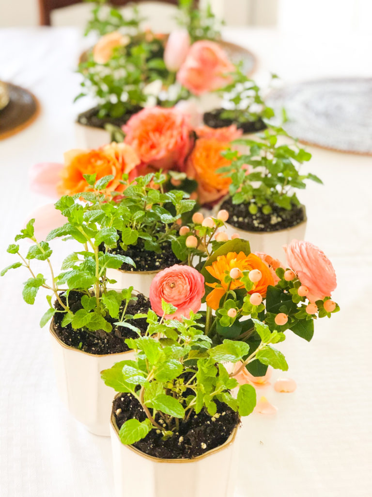 mint plants in white pots and orange flowers in vases alternating in center of table
