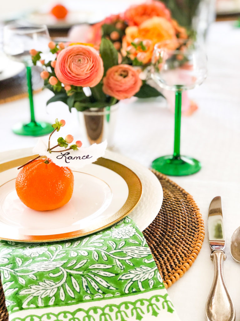 table setting with green napkin brown rattan place mat white and gold plates and orange flowers