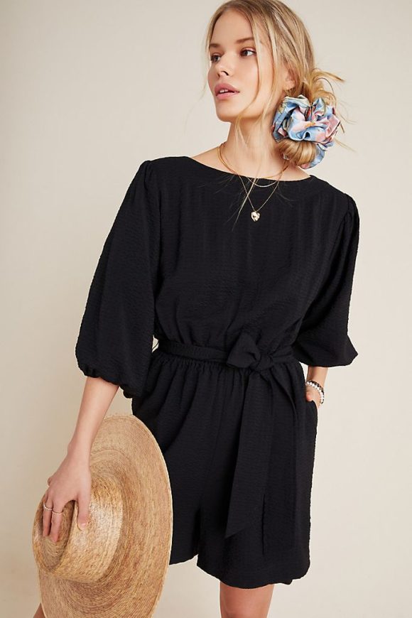 lady in black romper with balloon sleeves holding hat with hair in messy side bun with scrunchie