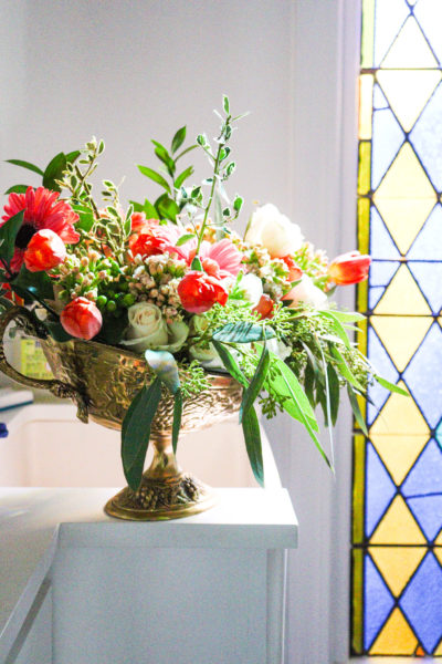 flower arrangement in brass container beside stain glass window