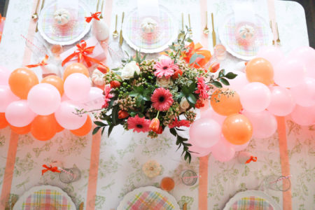 table setting in pink and orange with flowers and balloon garland centerpiece