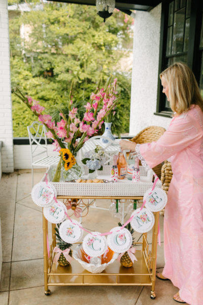 lady in long pink dress arranging items on bar cart