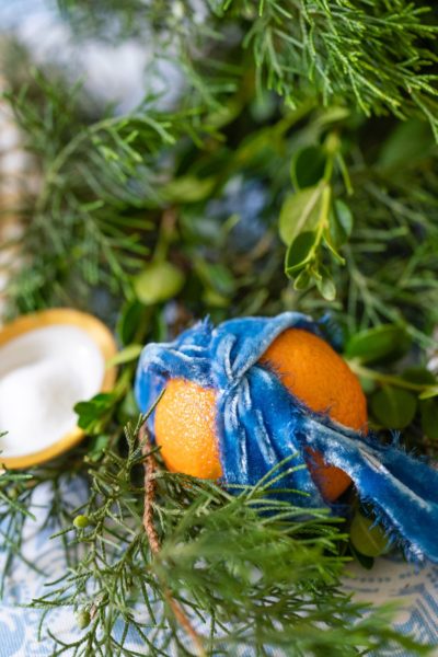 orange tied with blue velvet ribbon and placed in evergreens on a table centerpiece