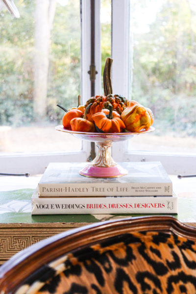 ornamental gourds in pink compote dish placed on stack of books in window